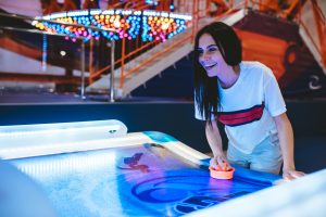 Attractive young woman is having fun in amusement park. Playing table hockey.