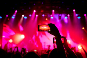 Smartphone in hand at a concert, red light from stage