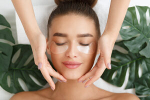 Woman with eye patches having face massage at beauty salon